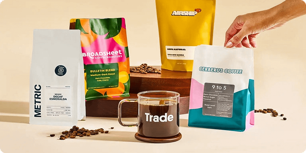 Specialty coffee subscription featuring Metric, Broadsheet, Airship, and Cerberus Coffee with Trade Coffee mug Assorted coffee bags from Metric, Broadsheet, Airship, and Cerberus Coffee displayed with a glass mug of Trade Coffee.
