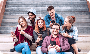 group of six young adults sitting on outdoor stairs, smiling and laughing while looking at their smartphones together